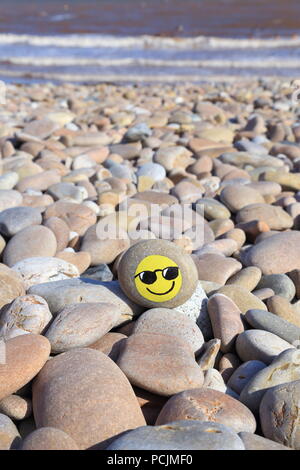 Pietra dipinta con faccina sorridente sulla spiaggia di ciottoli della Jurassic Coast in Devon Foto Stock