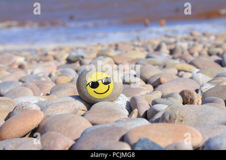 Pietra dipinta con faccina sorridente sulla spiaggia di ciottoli della Jurassic Coast in Devon Foto Stock