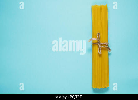 Bundle di italiano gli spaghetti legati con spago giacente su sfondo blu. Vista superiore Foto Stock