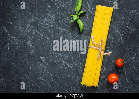 Bundle di italiano gli spaghetti legati con spago giacente sulla pietra scura sullo sfondo. Vista superiore e spazio di copia Foto Stock