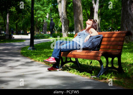 Redhead donna a prendere il sole nel parco e sedersi sul banco di lavoro Foto Stock