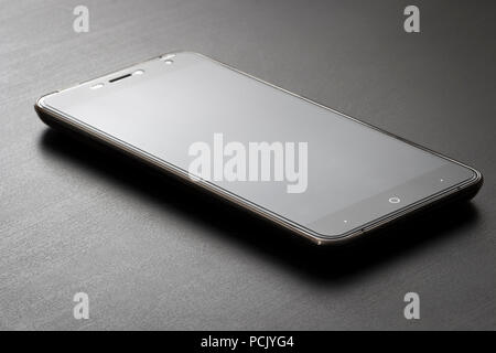 Uno smartphone si appoggia su un nero office desk close-up. Foto Stock