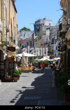 Un sacco di turisti passeggiando lungo la promenade a Procida, Italia, con case colorate dipinte in diverse tonalità pastello in background Foto Stock