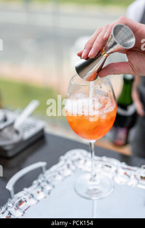 Barista rende cocktail Aperol spritz. Colmi di vetro, il fuoco selettivo. Bevanda alcolica basata sul banco bar con cubetti di ghiaccio e arance. parte esterna Foto Stock