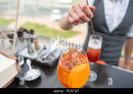 Barista rende cocktail Aperol spritz. Colmi di vetro, il fuoco selettivo. Bevanda alcolica basata sul banco bar con cubetti di ghiaccio e arance. parte esterna Foto Stock