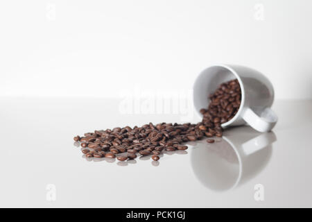 Molti caffè i chicchi di caffè la fuoriuscita di una tazza su un bianco con counterspace textspace e una riflessione Foto Stock