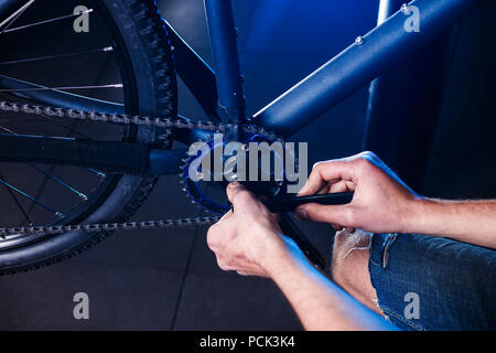 Un close-up di un maschio meccanico di bicicletta la mano in officina utilizza un utensile a cacciavite per regolare e riparare il gruppo pedivella per bicicletta, la bicicletta anteriore s Foto Stock