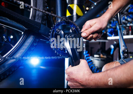 Un close-up di un maschio meccanico di bicicletta la mano in officina utilizza un utensile a cacciavite per regolare e riparare il gruppo pedivella per bicicletta, la bicicletta anteriore s Foto Stock