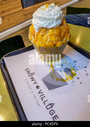 Rasatura Mango ghiaccio anche chiamato bingsoo alla rasatura coreano negozio di ghiaccio in Richmond, BC, Canada. Dolce di latte condensato viene aggiunto al ghiaccio rasata e guarnita con frutta fresca e panna montata. Foto Stock