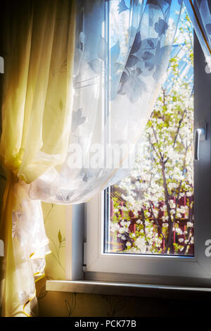 La vista dalla finestra di una casa privata in un giardino fiorito. Foto Stock