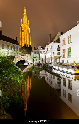 Vista della torre illuminata della chiesa di Nostra Signora a Bruges di notte con la riflessione in un canale. Foto Stock