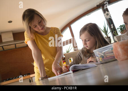 Madre aiutando i bambini con i compiti in cucina Foto Stock