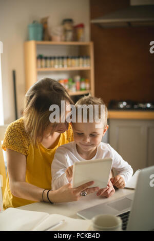 Madre e figlio seduti su una sedia con tavoletta digitale in cucina Foto Stock