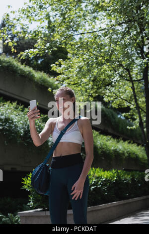 Donna sportivo facendo chiamata video sul telefono cellulare su strada Foto Stock