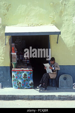 Arab Berger quotidiano di lettura al di fuori del tabaccaio e negozio di dolci a sud della Tunisia, Nord Africa Foto Stock