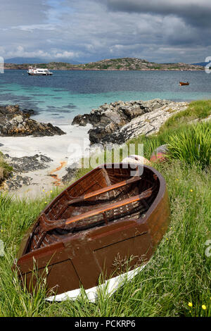 Spiaggia di sabbia e costa rocciosa di Isola di Iona con spiaggiata barca e vista di Isle of Mull montagne di ben più e tour in barca sul suono di Iona in Scozia Foto Stock