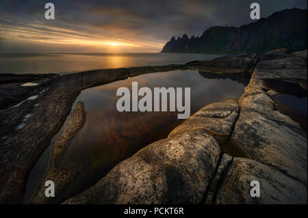 Tugeneset costa rocciosa con le montagne sullo sfondo al tramonto, Senja, Norvegia Foto Stock