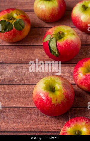 Fresche mele rosse con foglie verdi al buio su un sfondo di legno Foto Stock