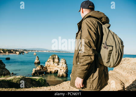 Un turista o viaggiatore con lo zaino si ammira la splendida vista dell'Oceano Atlantico e la costa vicino alla città chiamata Lagos in Portogallo. Foto Stock