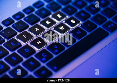 Falsa notizia scritta su un laptop con retroilluminazione tastiera close-up con messa a fuoco selettiva in un blu luce ambiente Foto Stock