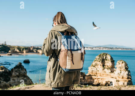 Un turista o viaggiatore con uno zaino passeggiate lungo la costa dell'Oceano Atlantico e si ammira la splendida vista dell'oceano vicino la città chiamata Lagos in Portogallo. Foto Stock