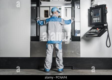 Grande macchina CNC Operatore. Caucasica lavoratore metalmeccanico nella parte anteriore della macchina. Foto Stock