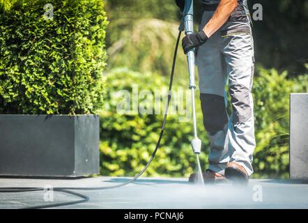 Il patio di pulizia a pressione. Uomini caucasici lavando il suo pavimento in calcestruzzo Patio con alte pressioni acqua detergente. Foto Stock