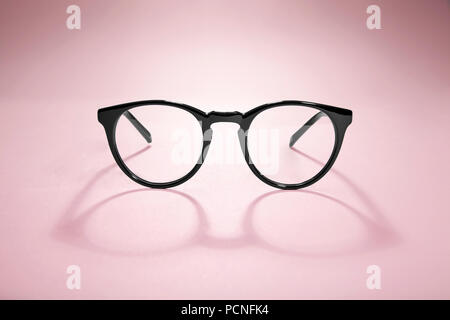 Studio shot di occhiali neri con lunga ombra a sfondo rosa. Foto Stock