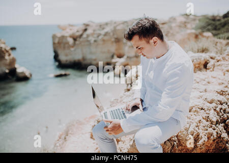 Vista laterale posteriore persona seduta azienda computer tavoletta ocean sunny sfondo naturale. Traveler divertirsi sul viaggio internazionale lifestyle, techn Foto Stock