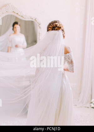 La vista del retro della sposa con il velo sulla testa guardando nello specchio. Foto Stock