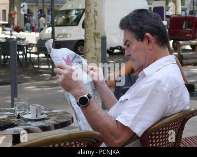 L'uomo rilassante mentre seduto fuori francese street cafe leggendo un giornale Foto Stock