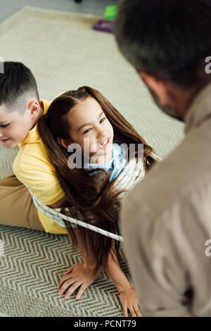 Elevato angolo di visione del padre dei bambini di legatura con corda a casa, la genitorialità concept Foto Stock