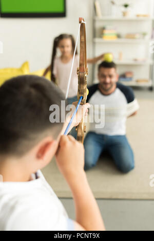 Messa a fuoco selettiva dei bambini che giocano con legato padre e fingere di tiro con arco giocattolo a casa Foto Stock