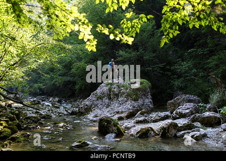 In estate sul fiume, giovane donna in piedi su una roccia durante le escursioni e attraversare un fiume incontaminato, Slovenia, Europa Foto Stock