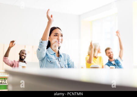 Felice giovani studenti alzando le mani per rispondere sulla questione degli insegnanti Foto Stock