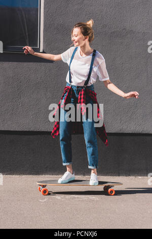 Vista laterale di felice giovane donna cavallo su skateboard Foto Stock