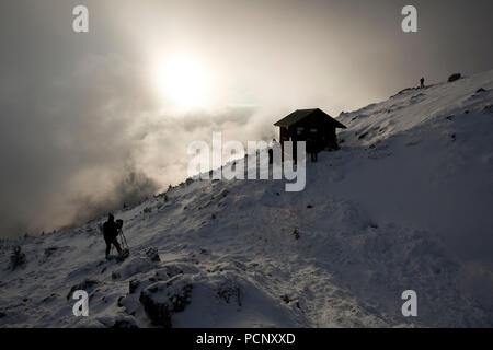 Escursionista sul Benediktenwand nella parte anteriore del bivacco Baita in inverno, Alpi Bavaresi, Alta Baviera, Baviera, Germania Foto Stock