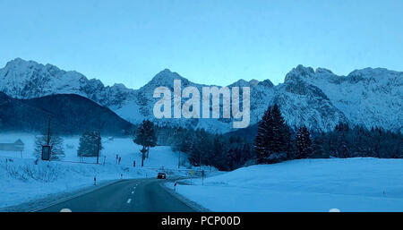 Coperte di neve paesaggio, street con auto che sopraggiungono di fronte montagne Karwendel durante il sunrise Foto Stock