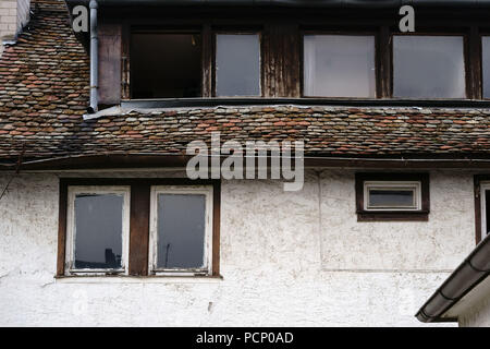 Pendente, fatiscente e nostalgico windows e tegole di un vecchio e un edificio elencato. Foto Stock