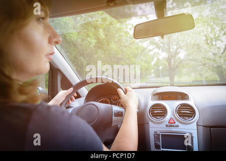 Donna alla guida di una vettura, la stretta di mano al volante. Vista da dietro Foto Stock