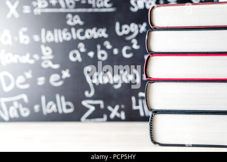 Pila e pila di libri di fronte a una lavagna nella scuola. Equazione matematica manoscritta su lavagna. Foto Stock