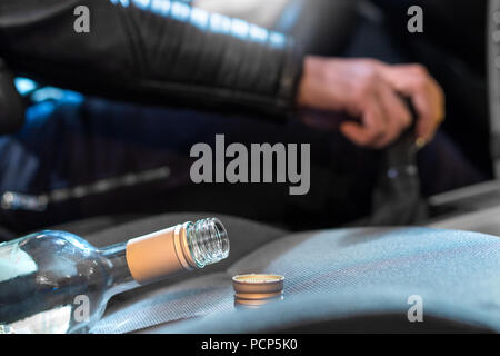 La guida in stato di ebbrezza concetto. Giovane uomo alla guida di auto sotto l'influenza di alcol. Mano sul cambio. Close up della bottiglia vuota di vino sul sedile anteriore. Foto Stock
