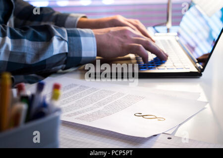 Avvocato lavoro in ufficio fino a tarda notte. Avvocato iscritto un documento legale con il computer portatile. Pezzi di carta con simbolo di giustizia. Foto Stock