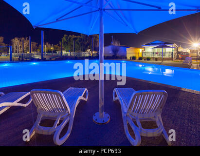 Sedie a sdraio sotto ombrellone vicino di lusso piscina nel parco vacanze di notte Foto Stock