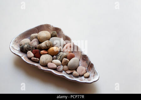 Mare pietre colorate in vari modelli all'interno di una lucida seashell isolato su sfondo bianco Foto Stock