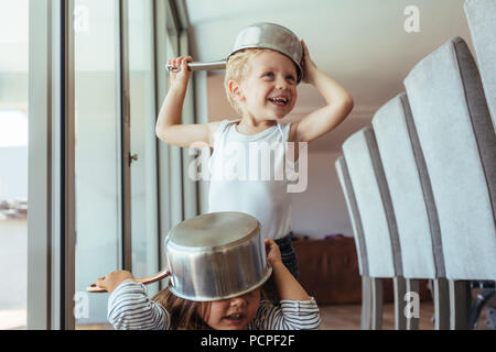 Sorridente giovane ragazzo e ragazza indossando ciotola come casco a casa. Bambini giocano knight con un arnese da cucina e divertimento. Foto Stock