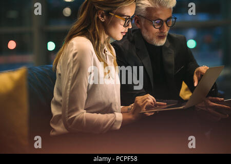 Imprenditrice con il suo capo seduto in ufficio e lavora sul computer portatile. Due uomini di affari che lavora fino a tardi in ufficio con la finitura di un progetto. Foto Stock