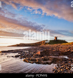 Il castello di Dunstanburgh, ora un rudere, comandando la spiaggia di Embleton Bay, Northumberland, Inghilterra, sotto una drammatica alba sky. Foto Stock