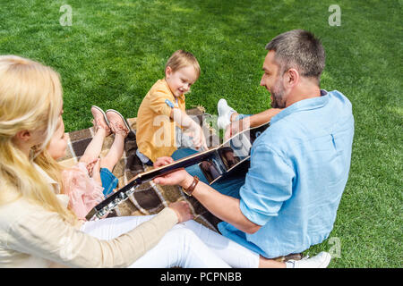 Padre Felice a suonare la chitarra mentre trascorrere il tempo con la famiglia in posizione di parcheggio Foto Stock