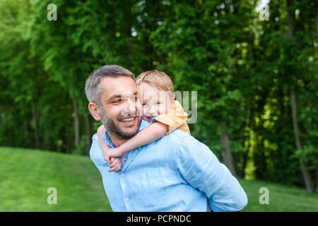 Padre Felice piggybacking adorabili poco figlio in posizione di parcheggio Foto Stock